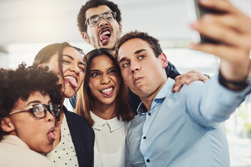 Poster - Try and look serious guys. Shot of a group of cheerful work colleagues taking a self portrait together inside of the office during the day.