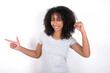© Roquillo - Young beautiful girl with afro hairstyle wearing grey t-shirt over white wall points at empty space holding fist up, winner gesture.