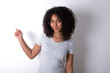 © Roquillo - Young beautiful girl with afro hairstyle wearing gray t-shirt over white wall points at copy space and advertises something, advices best price.