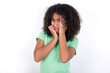 Doleful desperate crying Young beautiful girl with afro hairstyle wearing green t-shirt over white background , looks stressfully, frowns face, feels lonely and anxious