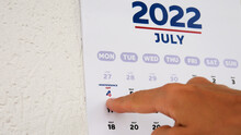 Close-up Of The Wall Calendar Page Of July 2022 With Marked Independence Day Date And A Male Hand Pointing Finger At It