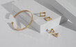 Modern gold bracelet and geometric earrings on white podium with copy space
