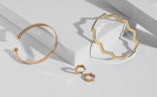 Two Modern Geometric Shape Golden Bracelets And Earrings Pair On White Podium With Copy Space