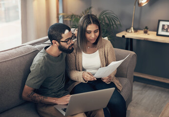 All hands on deck for creating a stable home. Shot of a young couple using a laptop while going through paperwork at home.