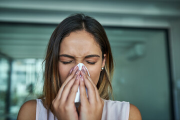 Wall Mural - These allergies are the worst. Shot of a young businesswoman blowing her nose in an office.