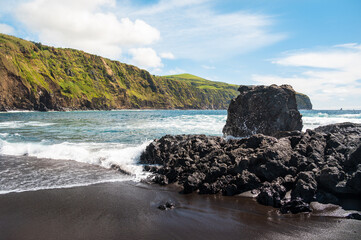 Ocean coast with black sand, volcanic sharp rocks and a beautiful green mountain on the horizon