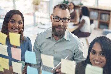 We get more done when we work together. Cropped portrait of a diverse group of businesspeople standing together and using a glass board to brainstorm in the office.