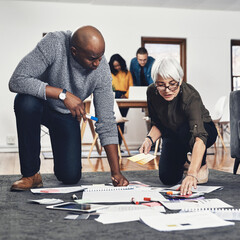 Poster - This method might just work. Full length shot of two businesspeople looking over paperwork while working on the floor of their office.