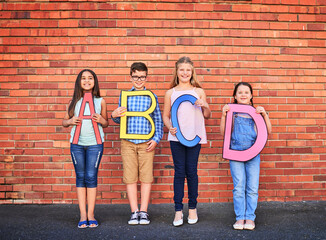 Sticker - The more you know, the more you grow. Portrait of a group of young children holding letters from the alphabet against a brick wall.