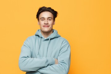 Wall Mural - a close horizontal photo of a handsome young man standing on an orange background in a light blue hoodie with his arms crossed over his chest