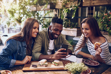 Poster - Want to see something funny. Shot of three friends looking at something on a cellphone while out for lunch.