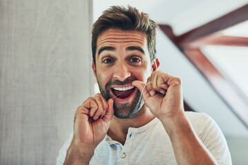 Poster - My teeth makes a great smile. Portrait of a cheerful young man flossing his teeth while looking at his reflection in the mirror at home.