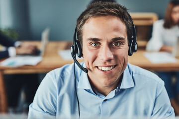 Aufkleber - He will help you over the phone. Portrait of a focussed young man talking to a customer over the phone while using a headset inside the office during the day.