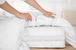 © New Africa - Woman putting blanket over soft white mattress on bed indoors, closeup