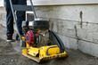 A close up image of a vibrating soil compactor being used to prepare soil for patio stones.