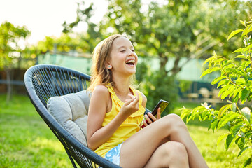 Happy kid girl playing game on mobile phone in the park outdoor