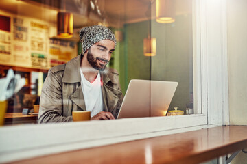 Canvas Print - Getting online at his local cafe. Shot of a handsome young man sitting at a cafe counter using a laptop.