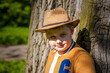 © Alina Lebed - Cute boy posing in a cowboy hat in the woods by a tree. The sun's rays envelop the space. Interaction history for the book. Space for copying