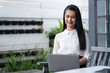 © amorn - Smiling Asian young woman using laptop computer at the outdoor office. Happy female working with laptop computer outdoor office.