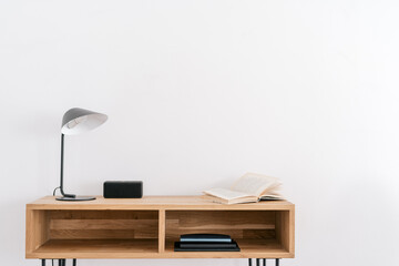 Open book and lamp on table near white wall