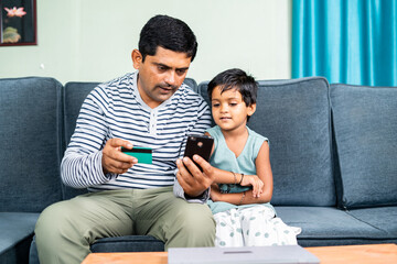 Father and daughter online shopping by using credit card payment on mobile phone at home - concept of relationship, wirless payment and e commerce.