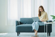 © ArLawKa - A freelance Asian woman working on a laptop checks social media while sitting on the sofa relaxing in her living room at home. concept of lifestyle for women