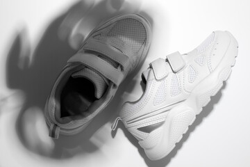 top view macro two white sneakers with hard summer sun shadows from a monstera on an isolated white background, one sneaker on the side.