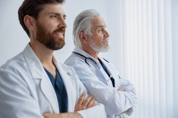 Wall Mural - Two doctors with crossing arms in uniform standing in medicine clinic hall and looking away