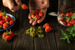 The chef prepares a sweet compote of fresh strawberries and mint on the kitchen table. Cook's hands while working