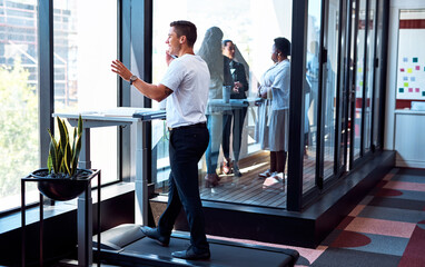 Poster - Theres no need to be deskbound as you head to success. Shot of a young businessman talking on a cellphone and going through paperwork while walking on a treadmill in an office.