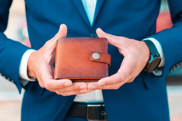 Man in a blue jacket shows off a leather brown wallet. Close-up of the hands. The concept of style and fashion