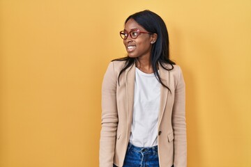 Poster - African young woman wearing glasses looking away to side with smile on face, natural expression. laughing confident.