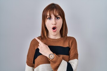 Poster - Young beautiful woman wearing striped sweater over isolated background surprised pointing with finger to the side, open mouth amazed expression.