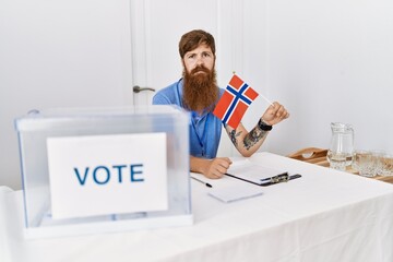 Wall Mural - Caucasian man with long beard at political campaign election holding norwegian flag thinking attitude and sober expression looking self confident