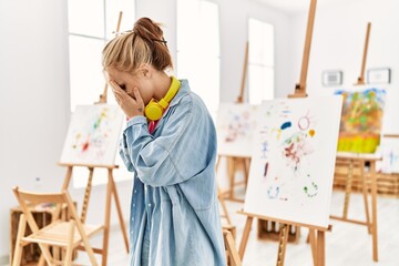 Canvas Print - Young caucasian girl at art studio with sad expression covering face with hands while crying. depression concept.