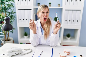 Wall Mural - Beautiful dentist woman holding ordinary toothbrush and electric toothbrush angry and mad screaming frustrated and furious, shouting with anger. rage and aggressive concept.