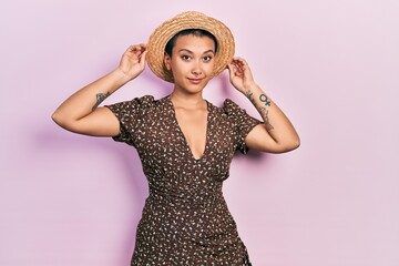 Wall Mural - Beautiful hispanic woman with short hair wearing summer hat relaxed with serious expression on face. simple and natural looking at the camera.