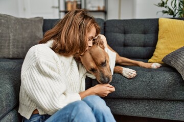 Poster - Young caucasian woman kissing and hugging dog sitting on floor at home