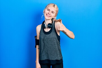 Poster - Beautiful caucasian woman with blond hair wearing sportswear doing happy thumbs up gesture with hand. approving expression looking at the camera showing success.