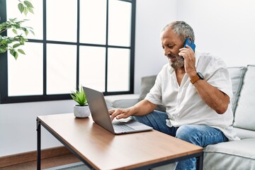 Sticker - Senior grey-haired man talking on the smartphone using laptop at home