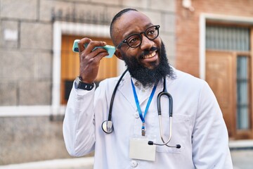 Poster - Young african american man wearing doctor uniform listening audio message by the smartphone at hospital