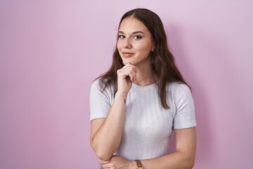 Sticker - Young hispanic girl standing over pink background with hand on chin thinking about question, pensive expression. smiling and thoughtful face. doubt concept.