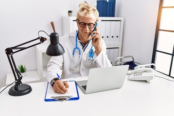 Poster - Young caucasian man wearing doctor uniform talking on the smartphone at clinic