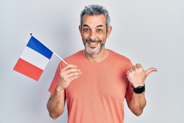 Poster - Handsome middle age man with grey hair holding france flag pointing thumb up to the side smiling happy with open mouth