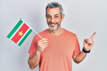 Poster - Handsome middle age man with grey hair holding suriname flag smiling happy pointing with hand and finger to the side