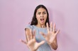 Young brazilian woman wearing casual t shirt over pink background afraid and terrified with fear expression stop gesture with hands, shouting in shock. panic concept.