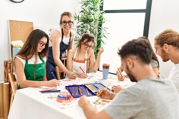 Group of young paint students smiling happy and drawing sitting on the table at art studio.