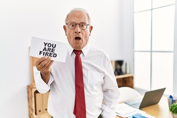 Poster - Senior business man holding you are fired banner at the office scared and amazed with open mouth for surprise, disbelief face