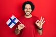 © Krakenimages.com - Handsome hispanic man holding finland flag doing ok sign with fingers, smiling friendly gesturing excellent symbol