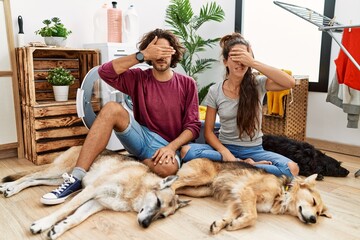 Wall Mural - Young hispanic couple doing laundry with dogs covering eyes with hand, looking serious and sad. sightless, hiding and rejection concept